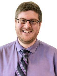 Jon, our Client Services Project Coordinator, is brightly smiling towards the camera and wearing a purple button-up shirt with a striped tie.